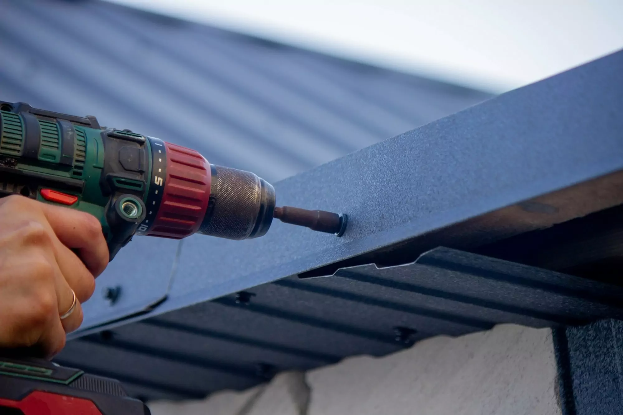 a man repairs the roof, tightens the self-tapping screw with a screwdriver